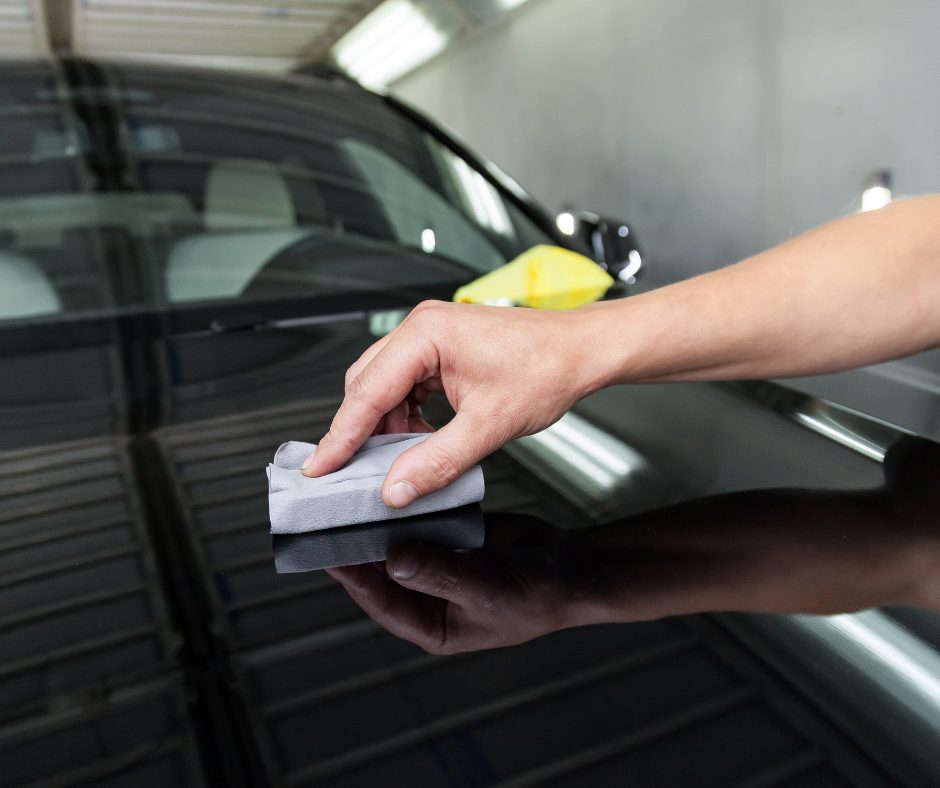 A person is polishing a black car with a sponge