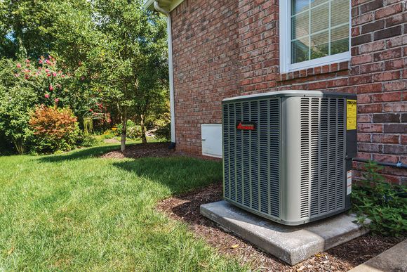 Two air conditioners are sitting in the grass in front of a brick building.