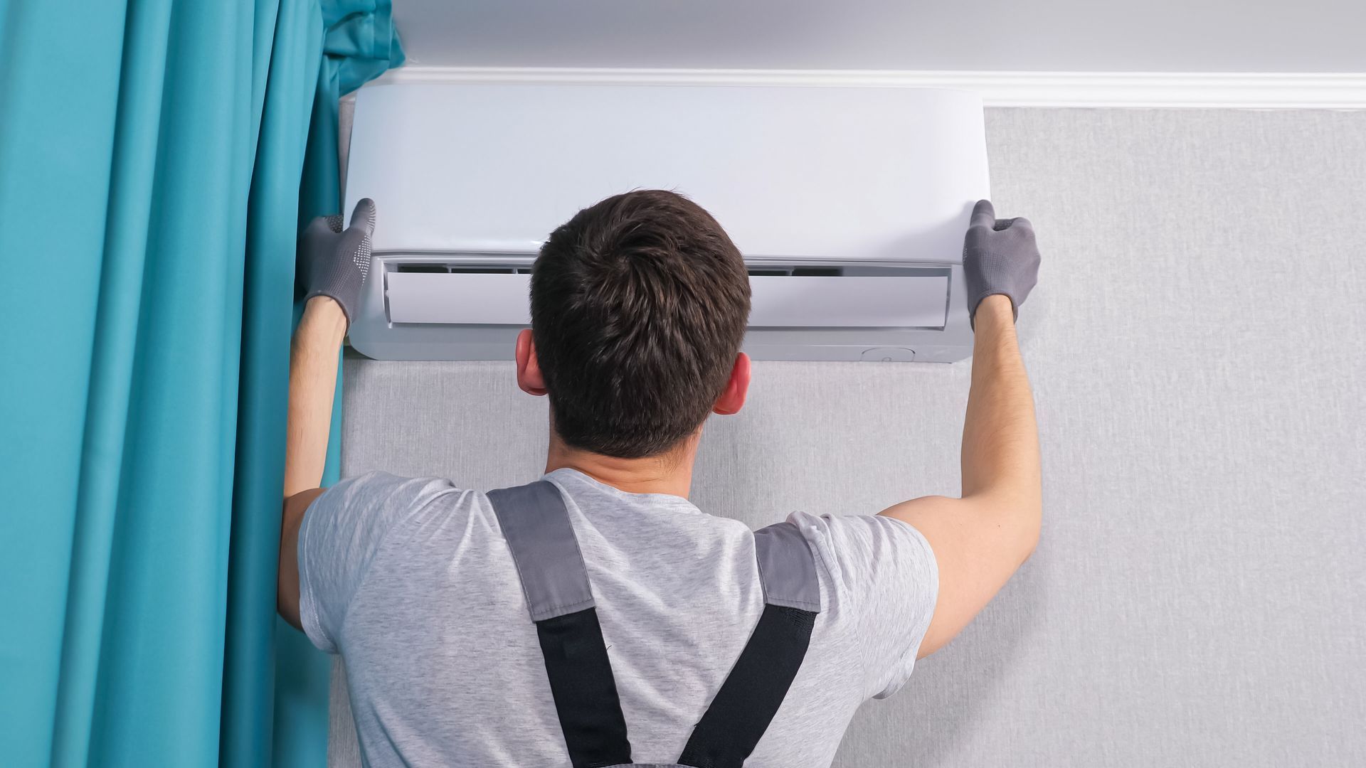 A man is installing an air conditioner on a wall.