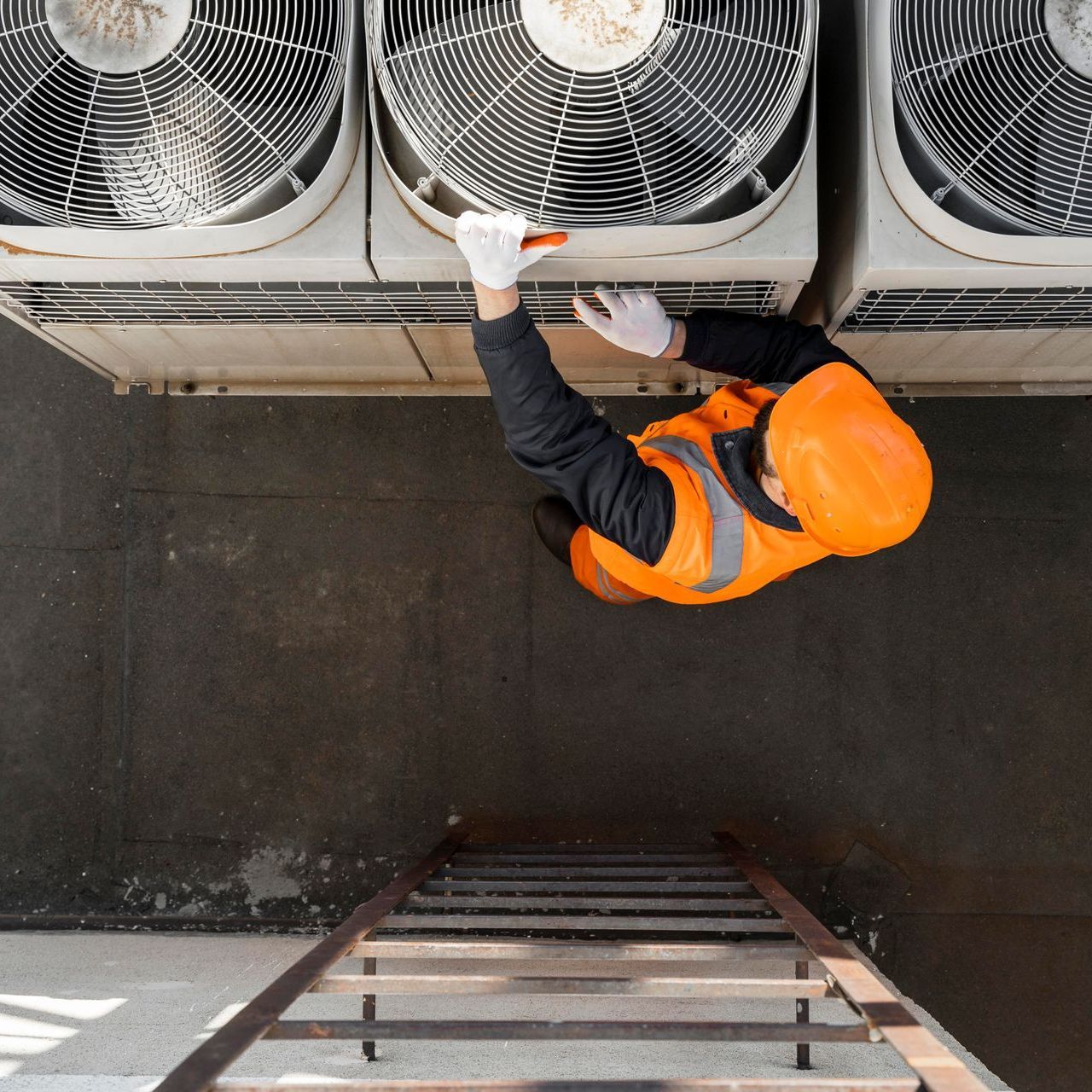 An aerial view of a man on a ladder working on air conditioners