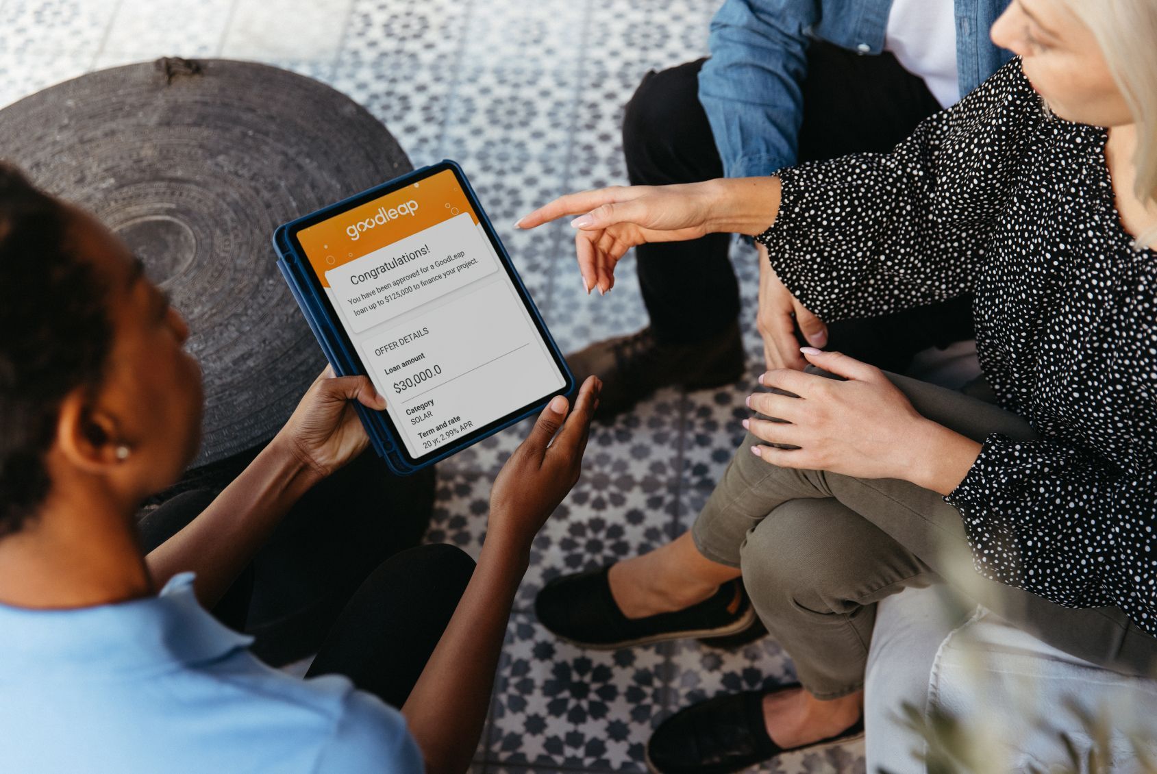 A group of people are sitting around a table looking at a tablet.