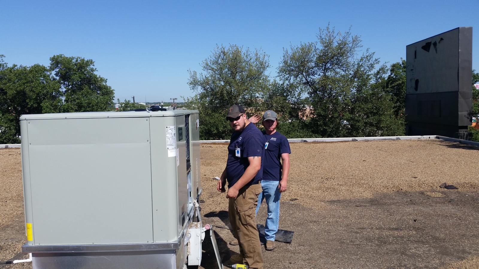 Two men are working on a rooftop air conditioner.