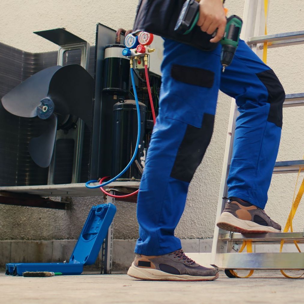 A man in blue pants is standing on a ladder holding a drill