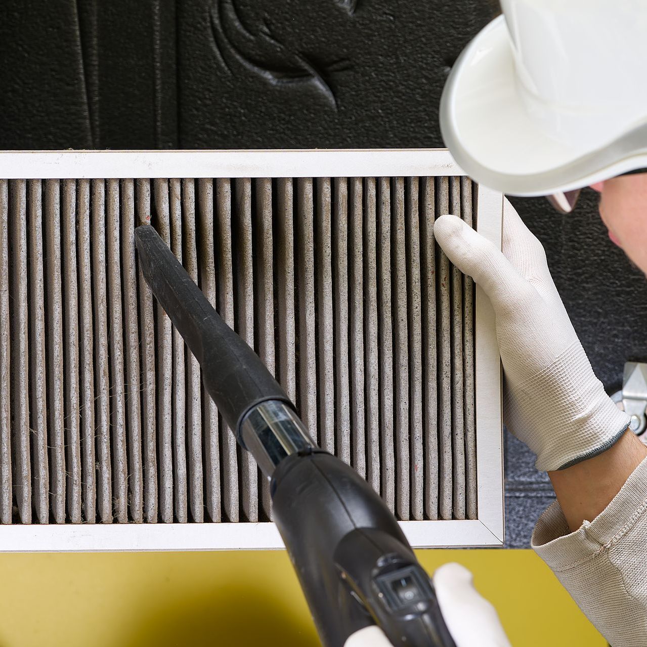 A person wearing gloves is using a vacuum cleaner to clean a filter