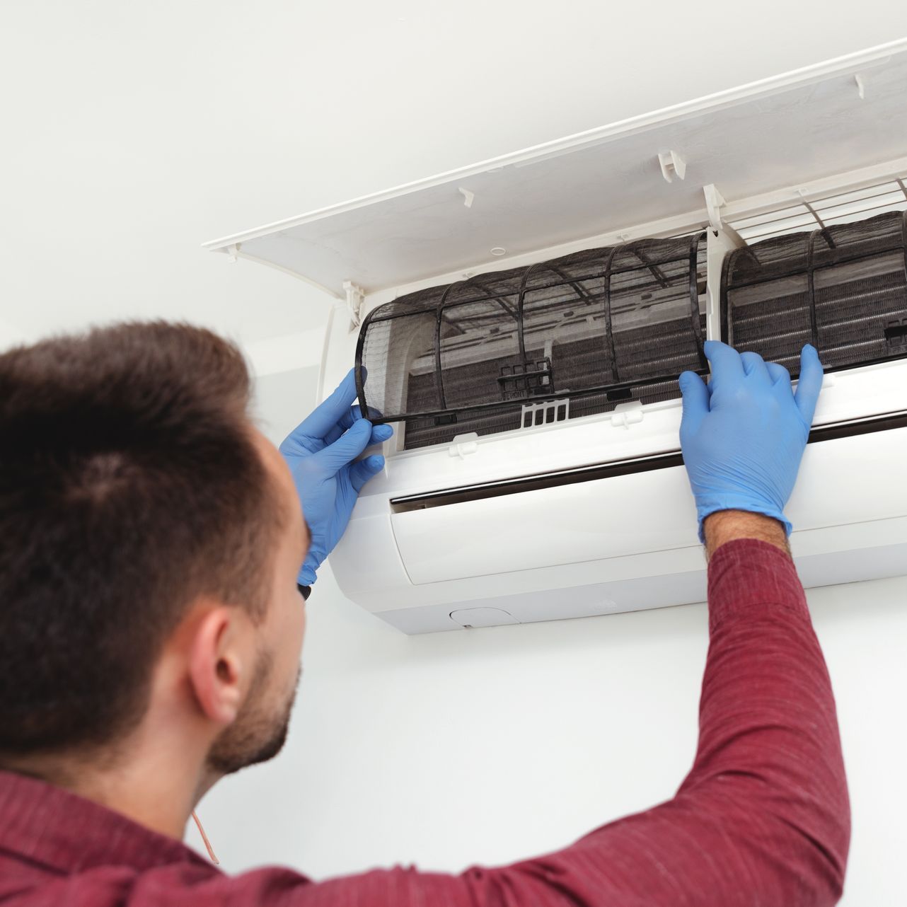 A man is cleaning an air conditioner with a magnifying glass.