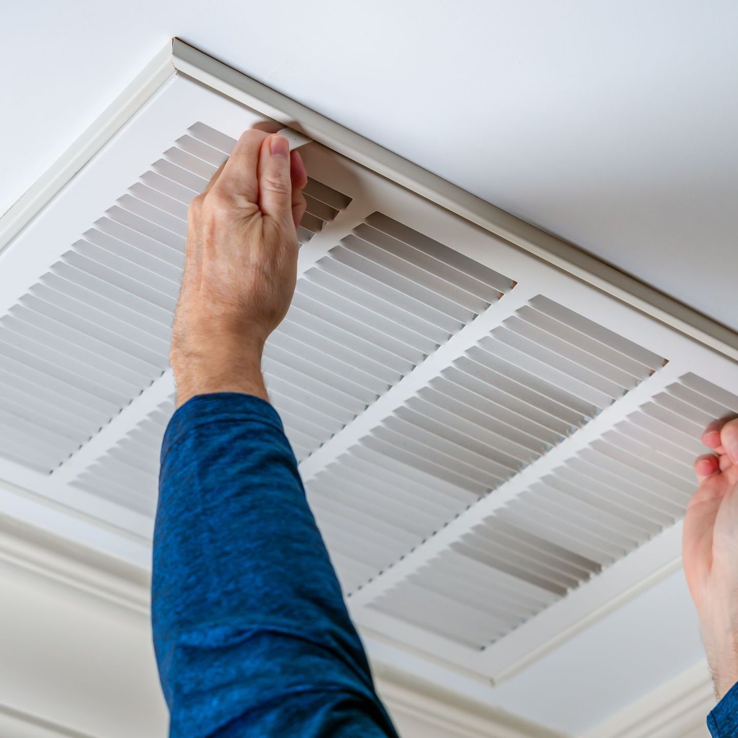 A person in a blue shirt is fixing an air vent on the ceiling