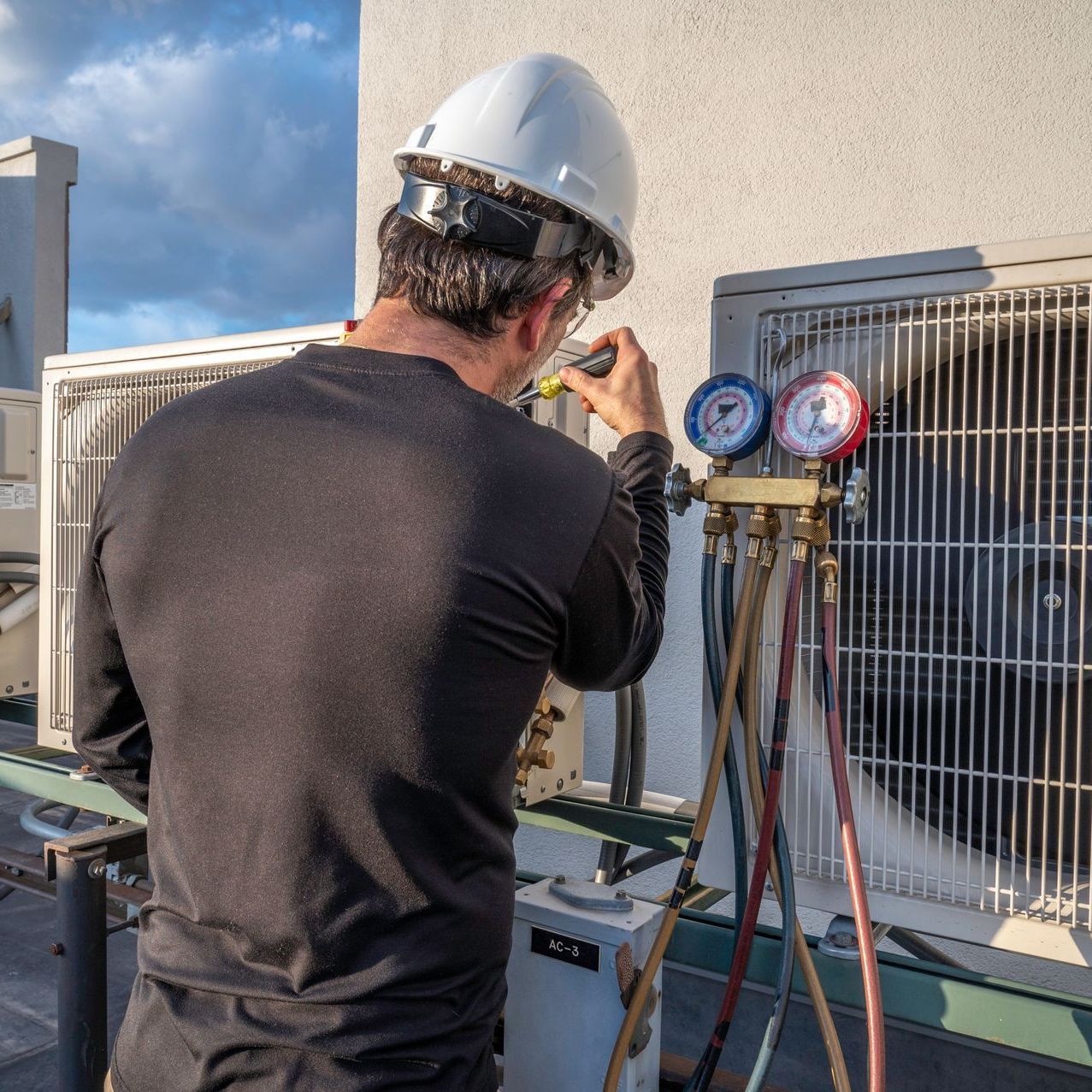 A man wearing a hard hat is working on an air conditioner