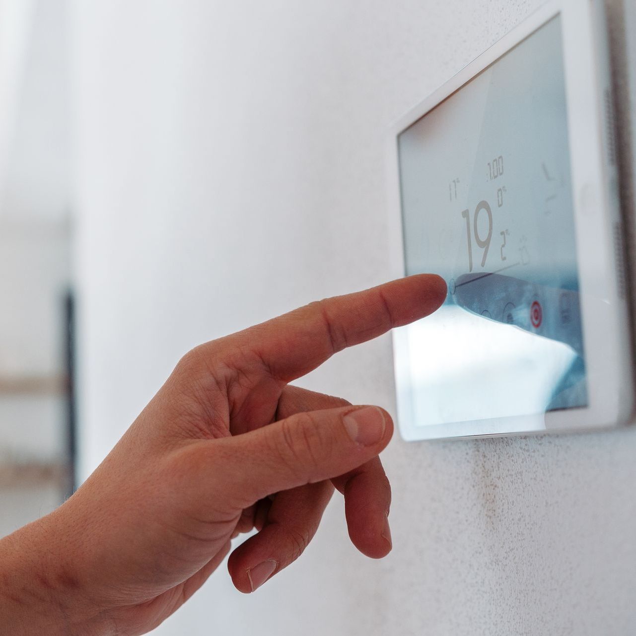 A person is pressing a button on a thermostat with their finger.