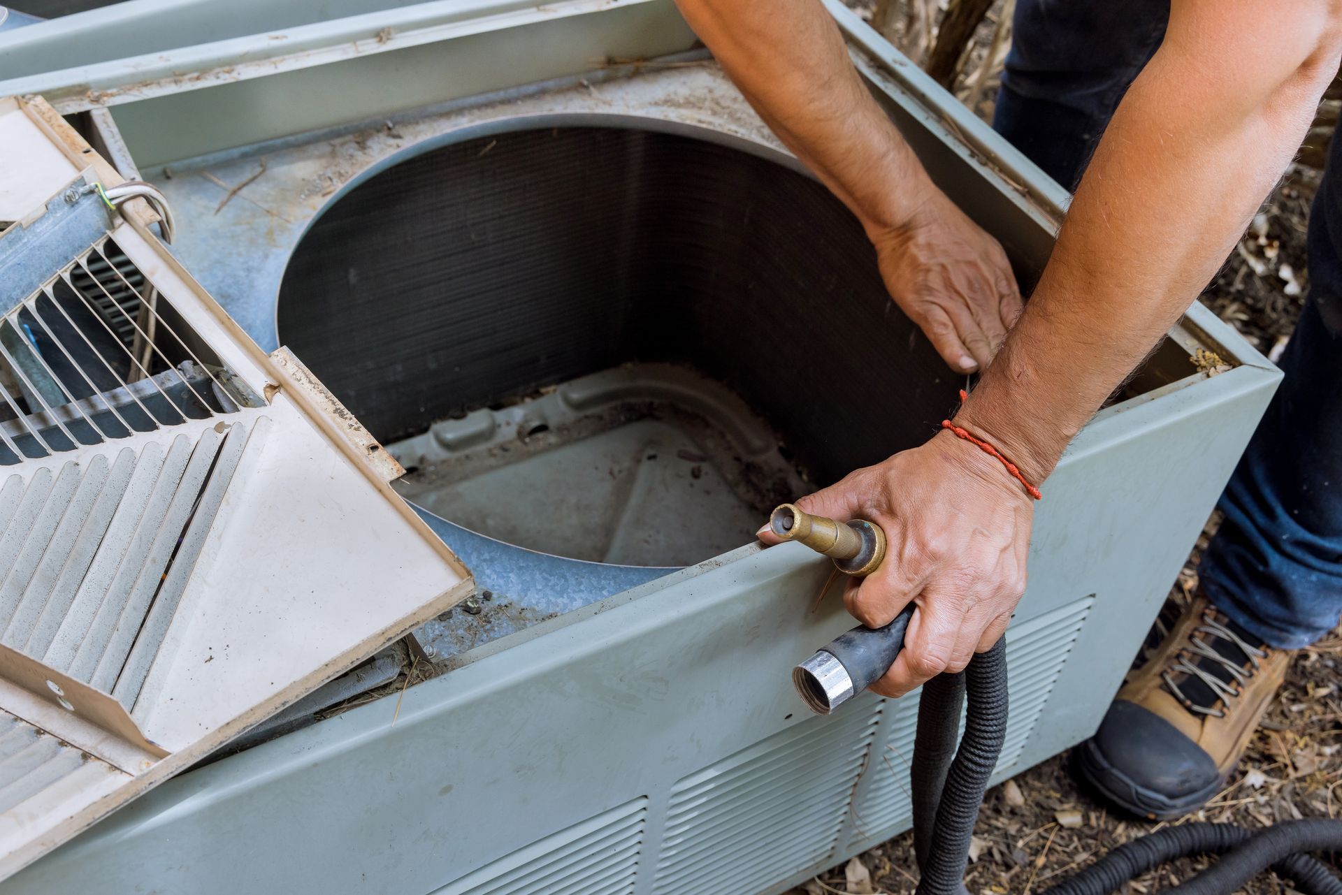 A man is cleaning an air conditioner with a hose.
