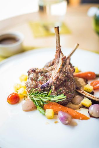 Rack of lamb with roasted vegetables on a white plate.