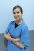 Woman in blue scrubs with arms crossed, in a medical setting, smiling.