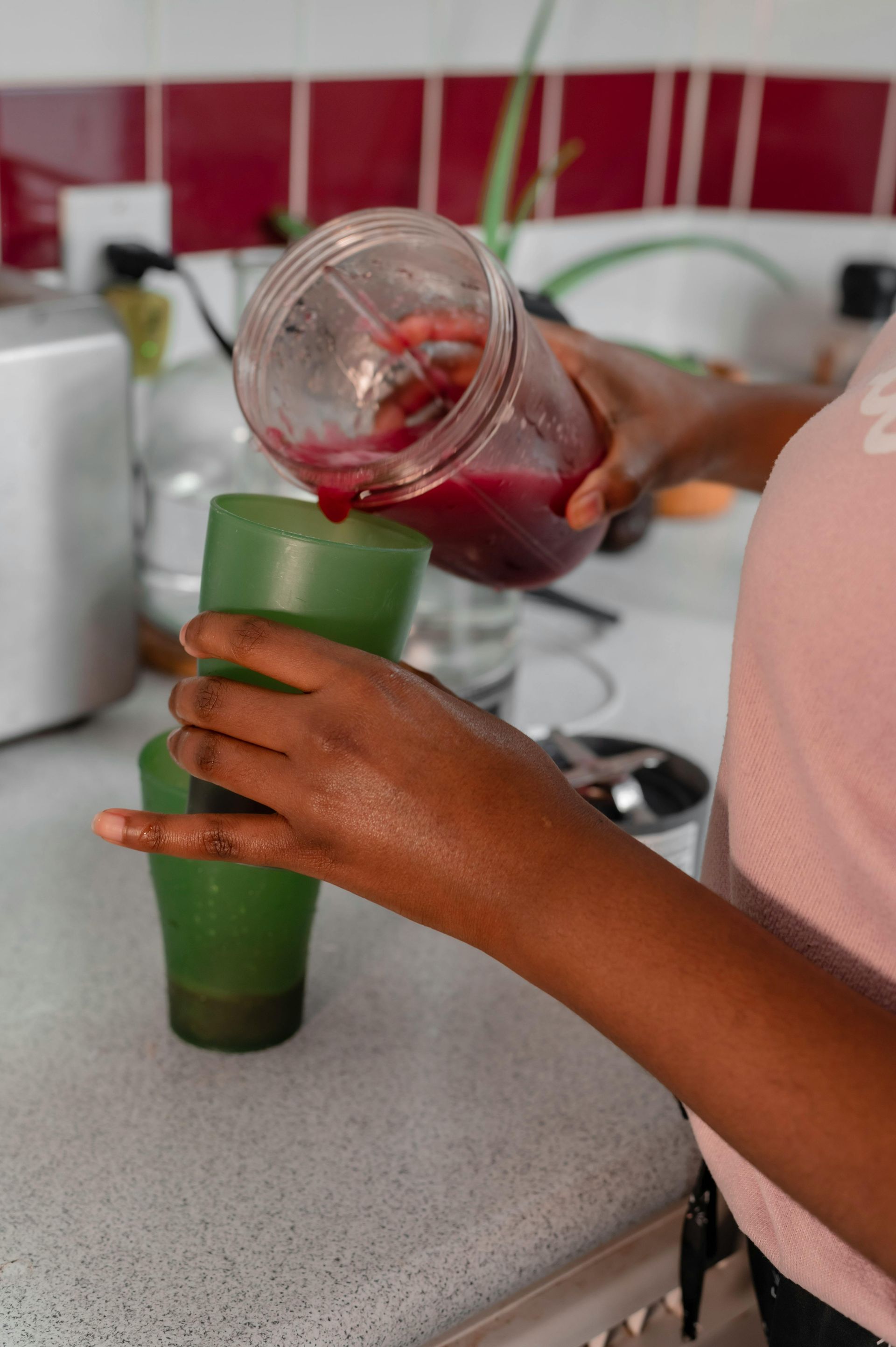 Person pouring purple juice from a blender into two green cups on a countertop.