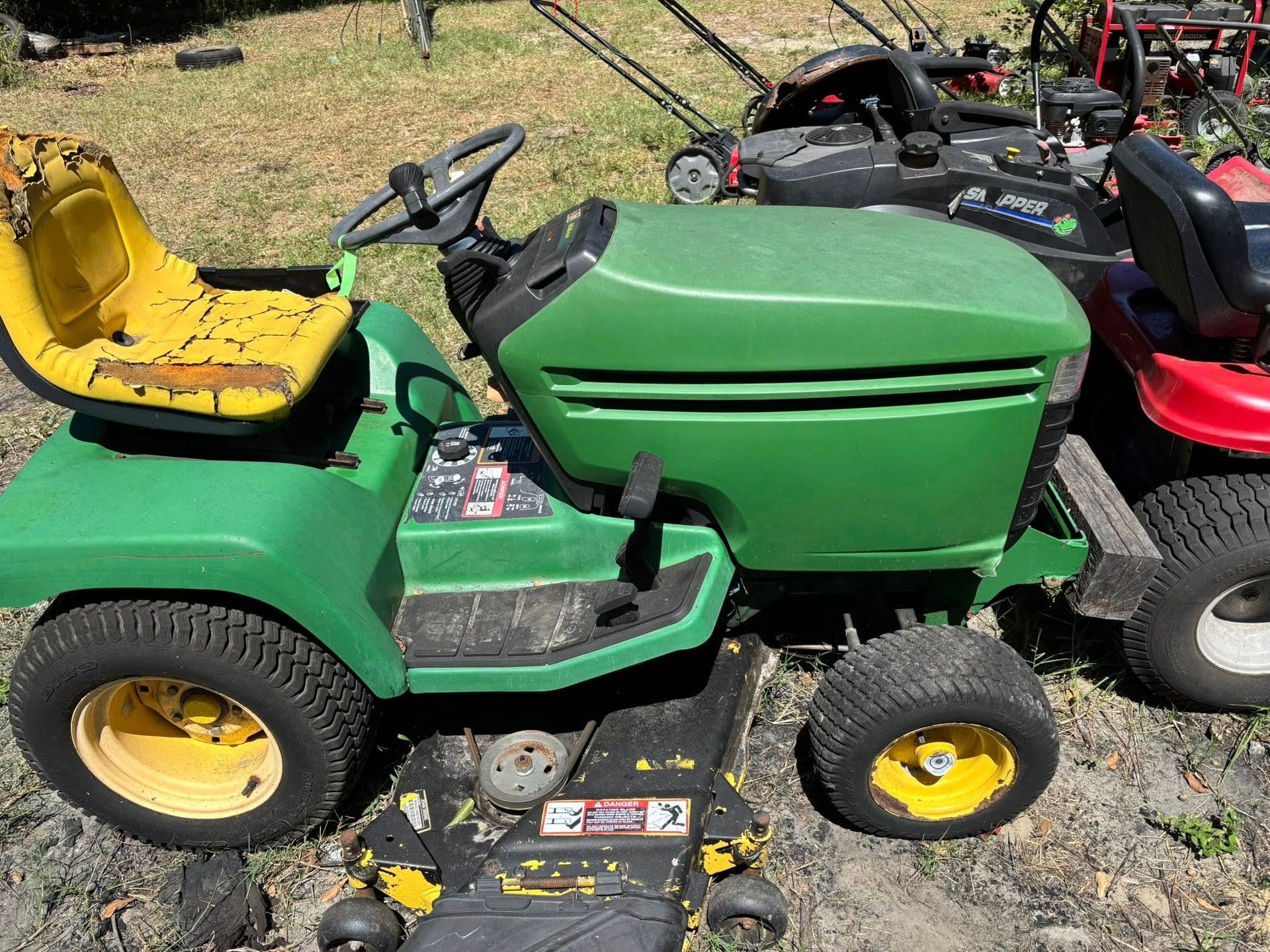 Green John Deere riding lawnmower with a yellow seat and wheels. Other lawnmowers are visible in the background.