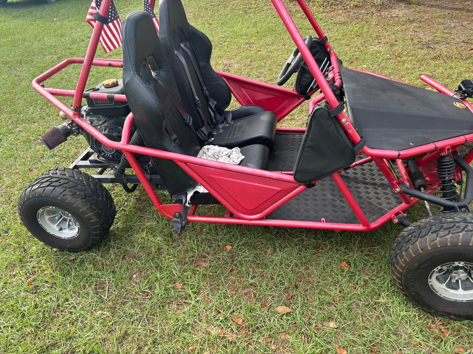 Red go-kart with black seats and an American flag. It sits on green grass.