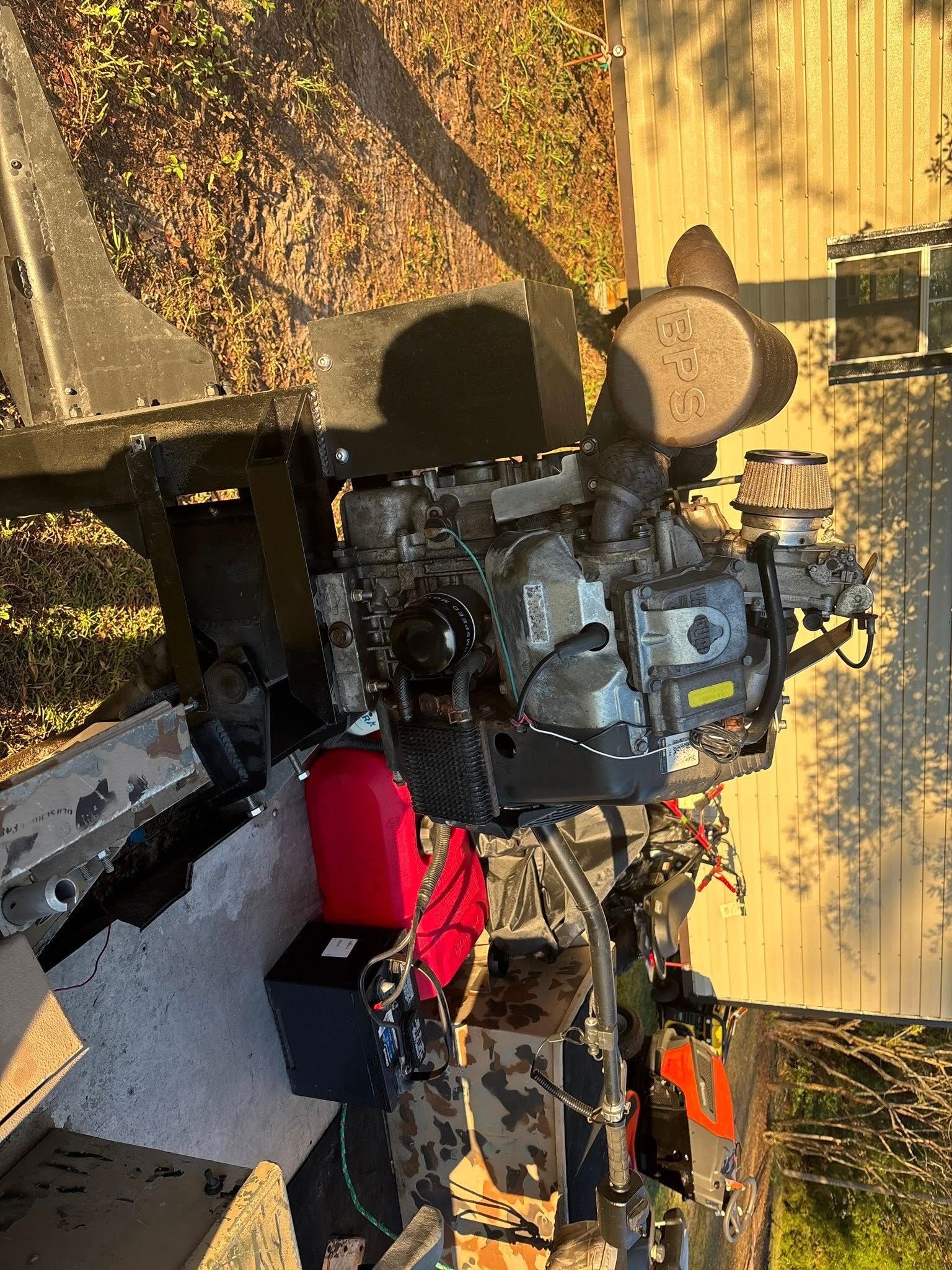 Engine on a metal frame, likely for a boat, with various attached components and a red fuel tank.