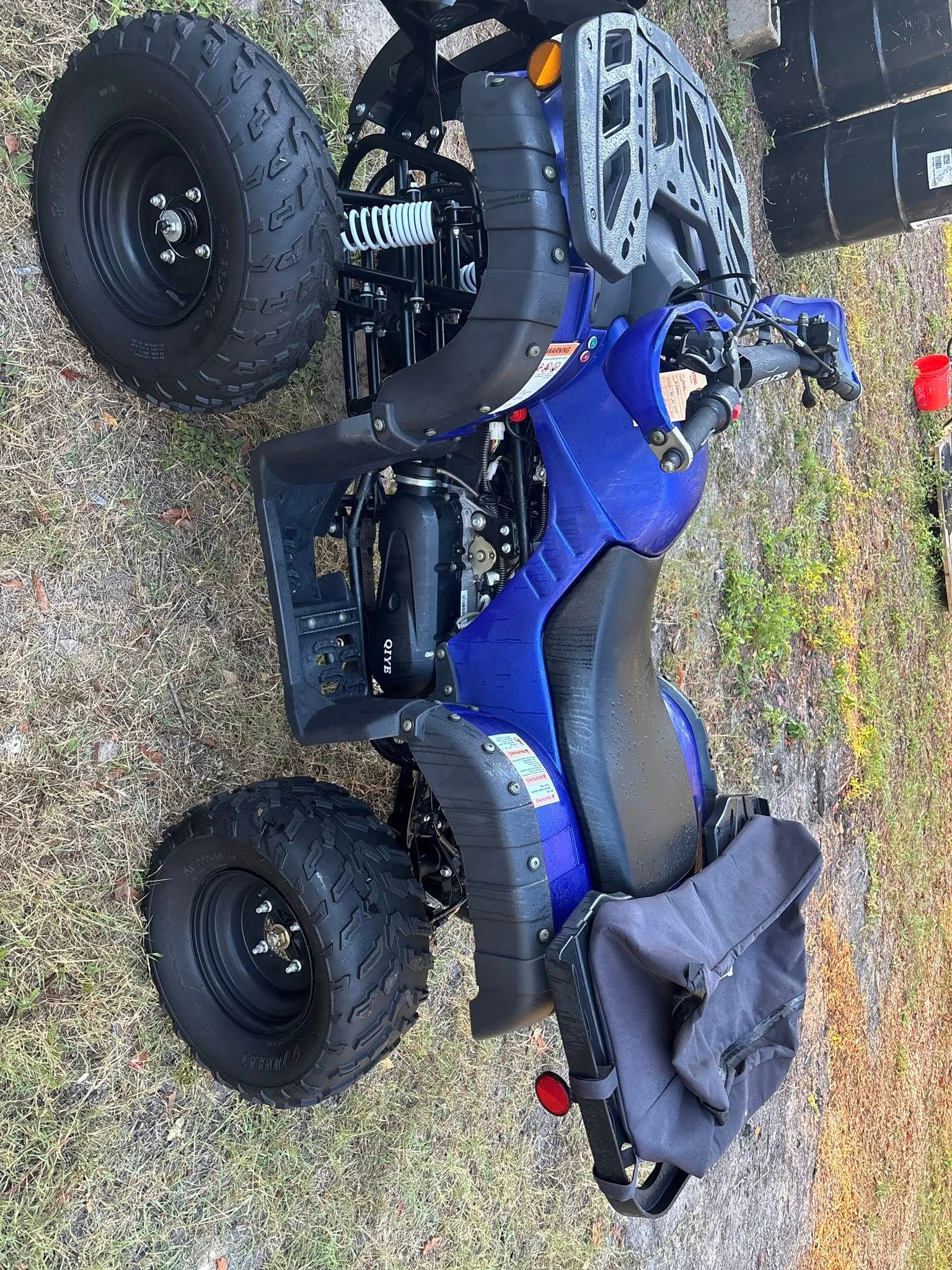 Blue and black ATV with large tires, parked outdoors.