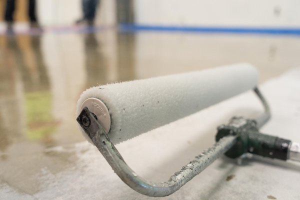 Paint roller applying white coating to a concrete floor.