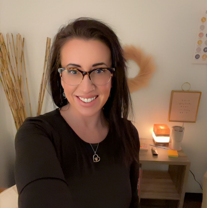 Smiling woman with glasses in a cozy room beside a lit candle and wall decor