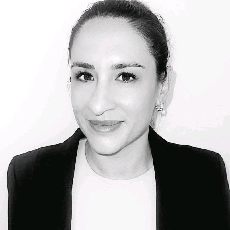 Portrait of a smiling person in a black blazer and white shirt against a light background