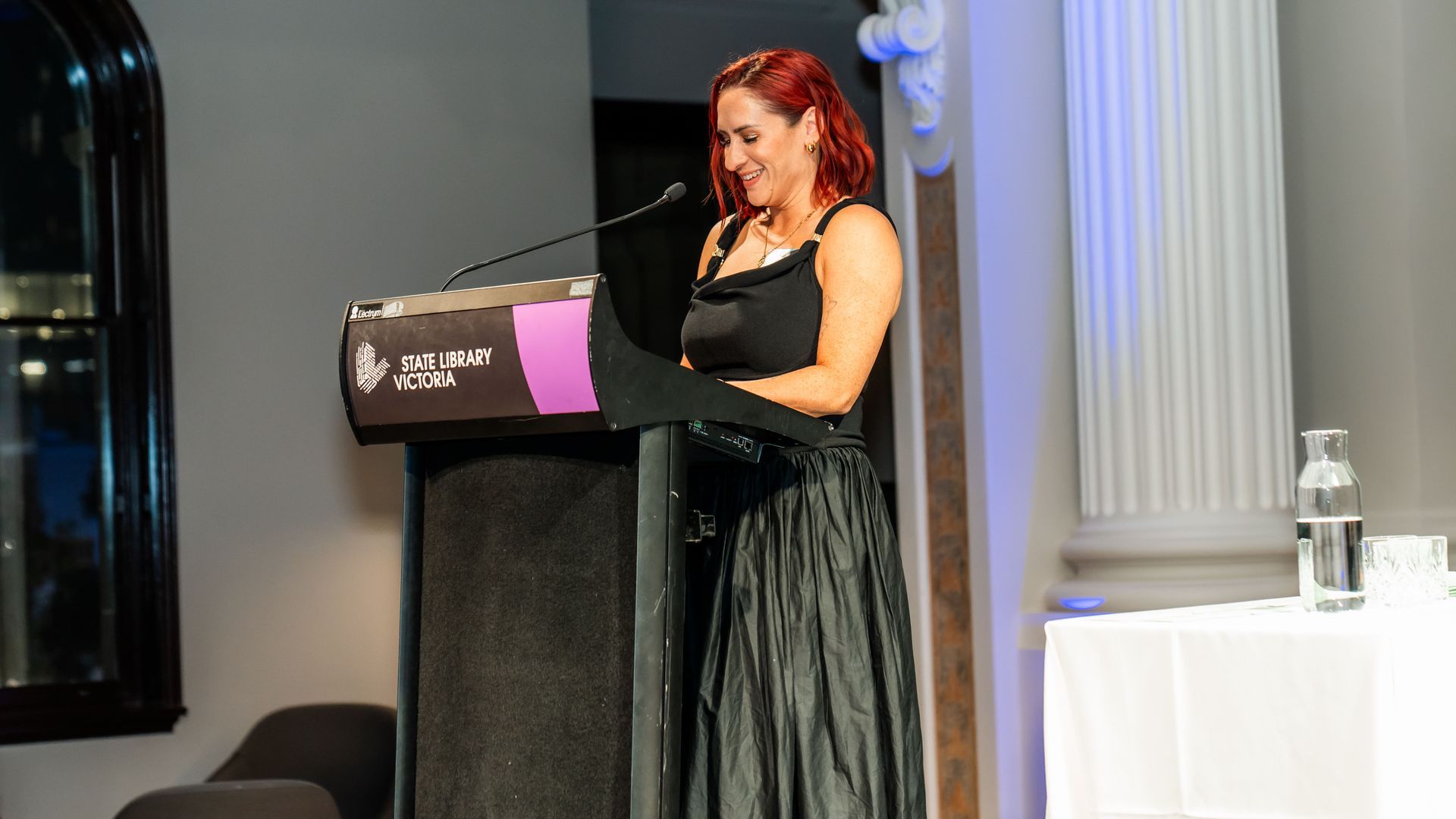 Woman in a black dress speaking at a podium on a stage