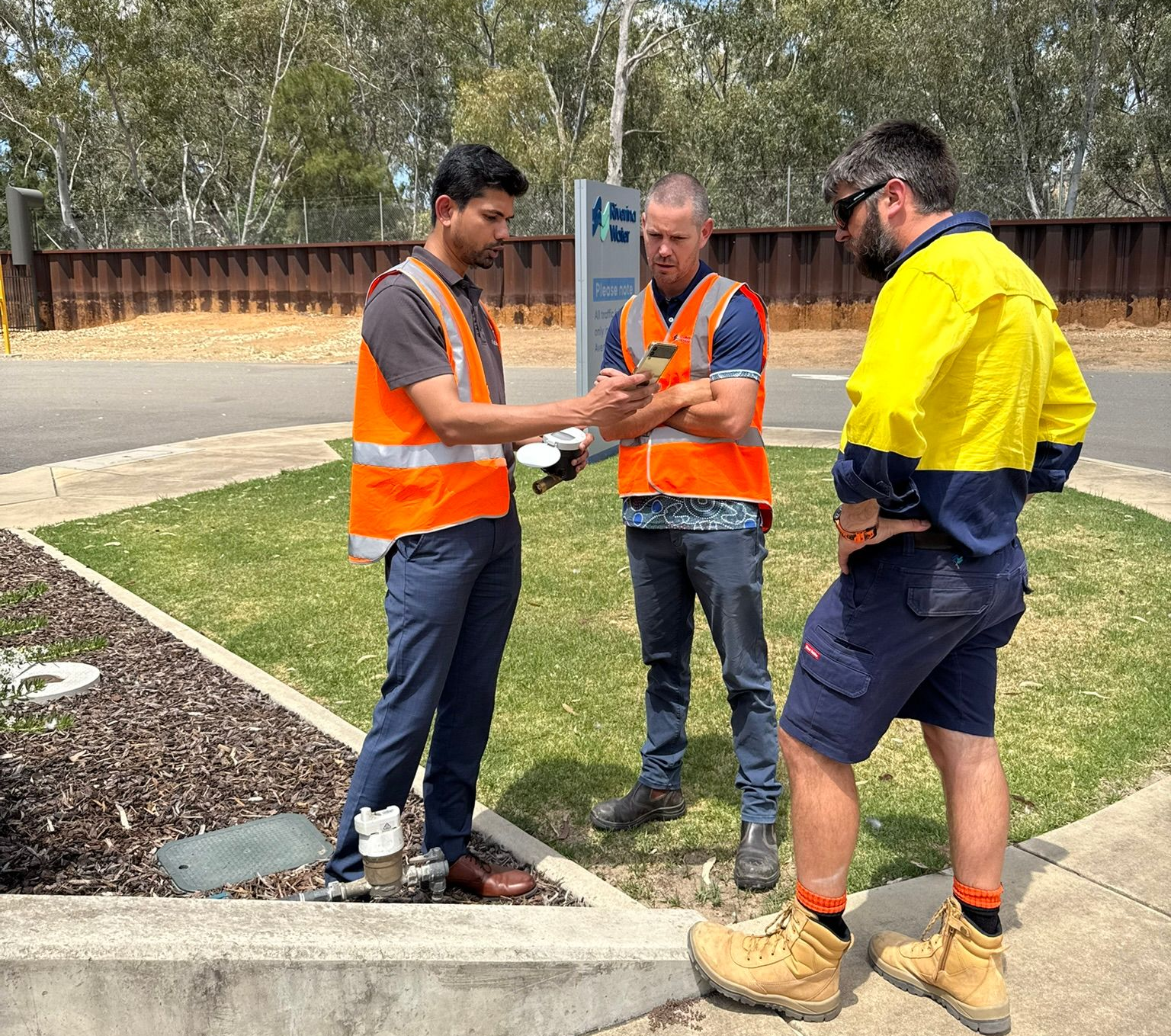 Three workers in safety vests review plans outdoors at a construction site.