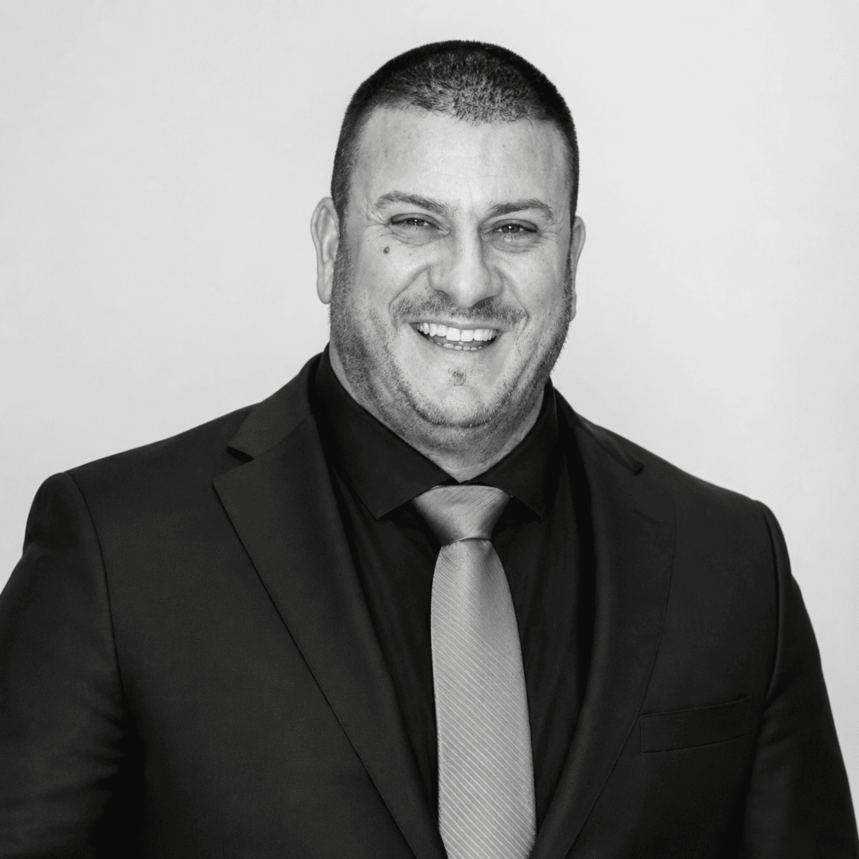 Portrait of a smiling man in a dark suit and polka-dot tie on a white background