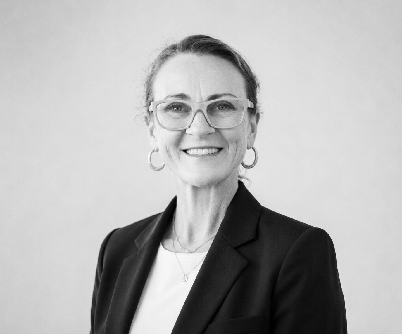Portrait of a smiling person in glasses wearing a dark blazer against a light background