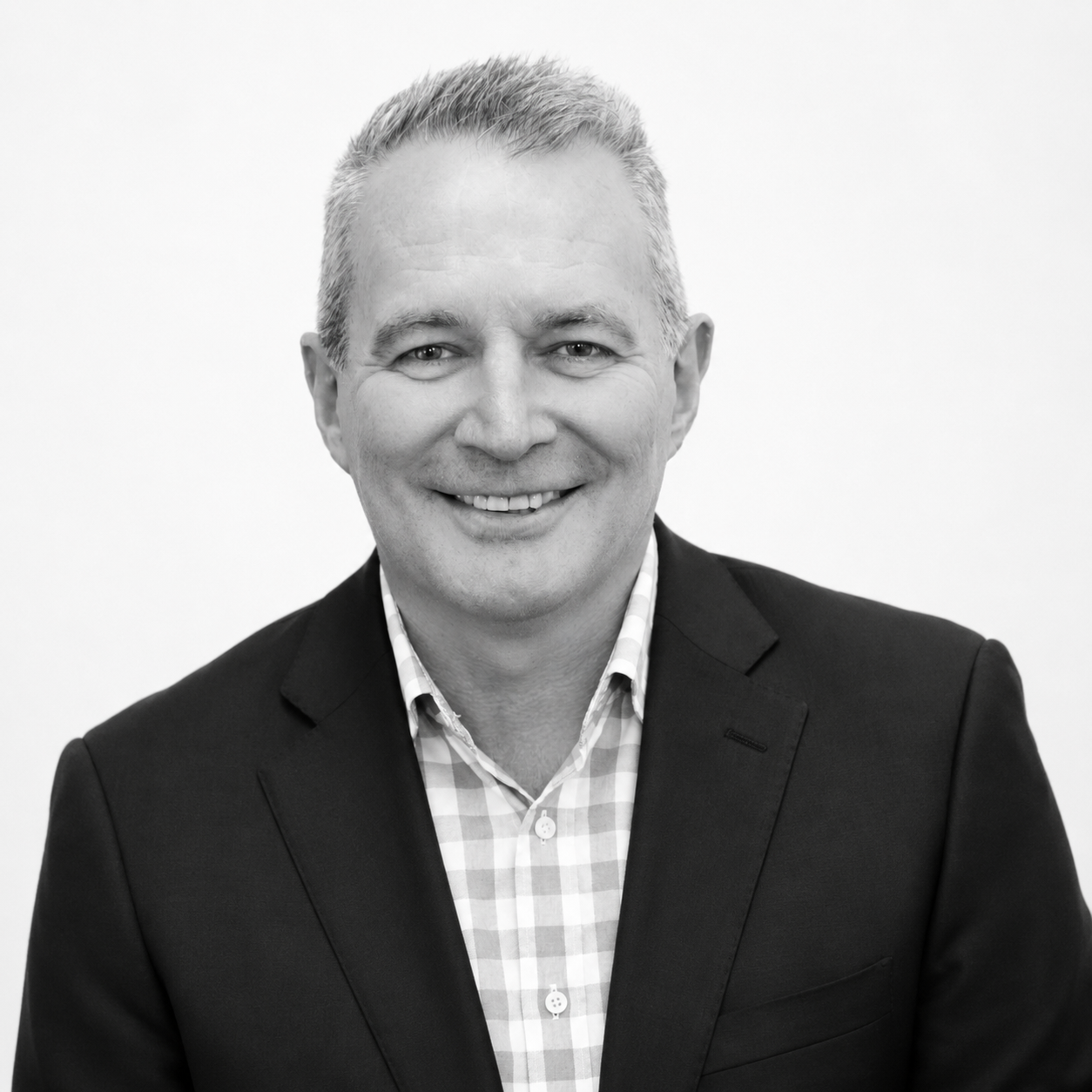 Smiling man in a dark blazer and checkered shirt against a white background