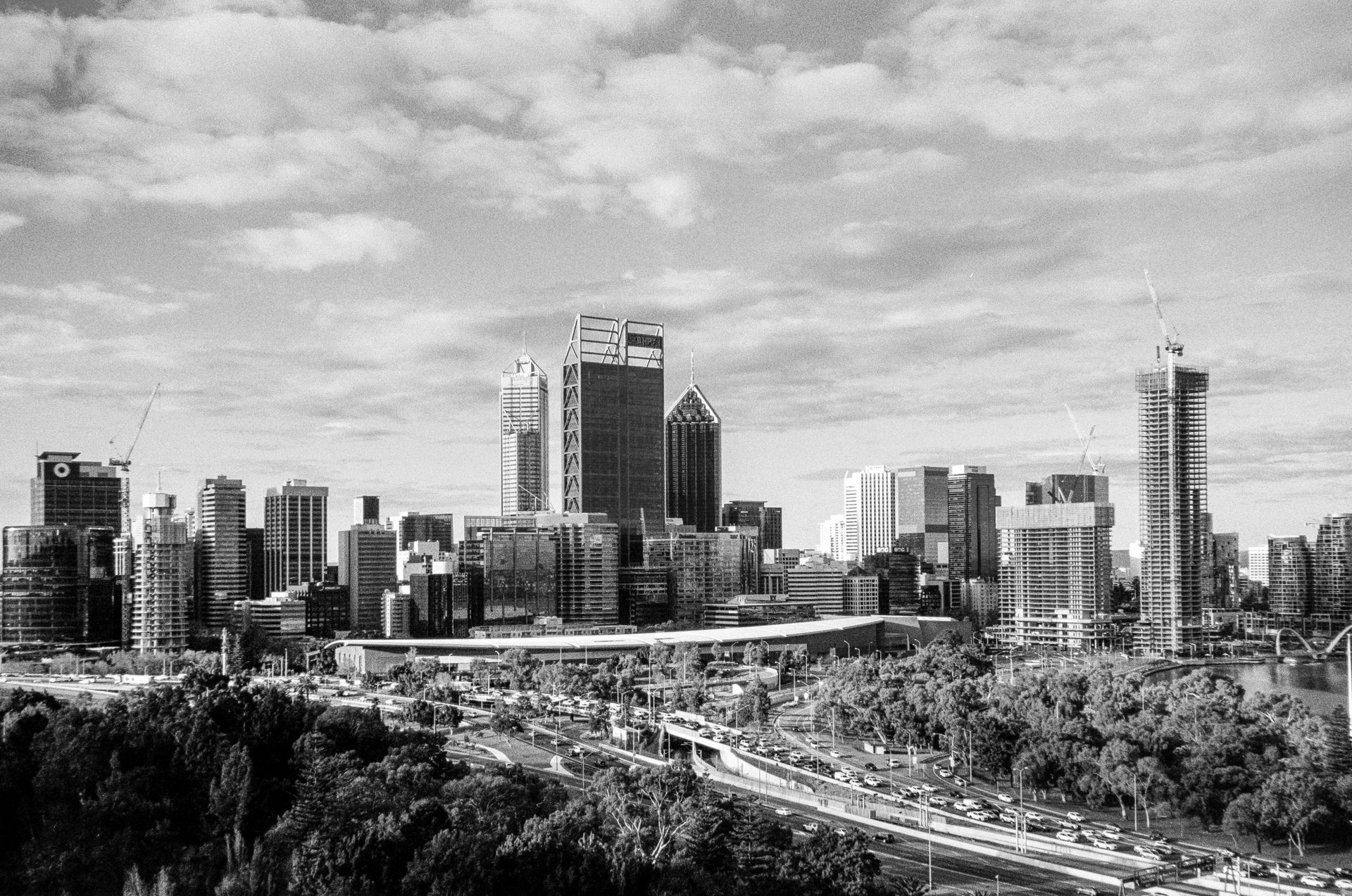 Black-and-white city skyline with high-rise buildings and a winding highway under cloudy skies