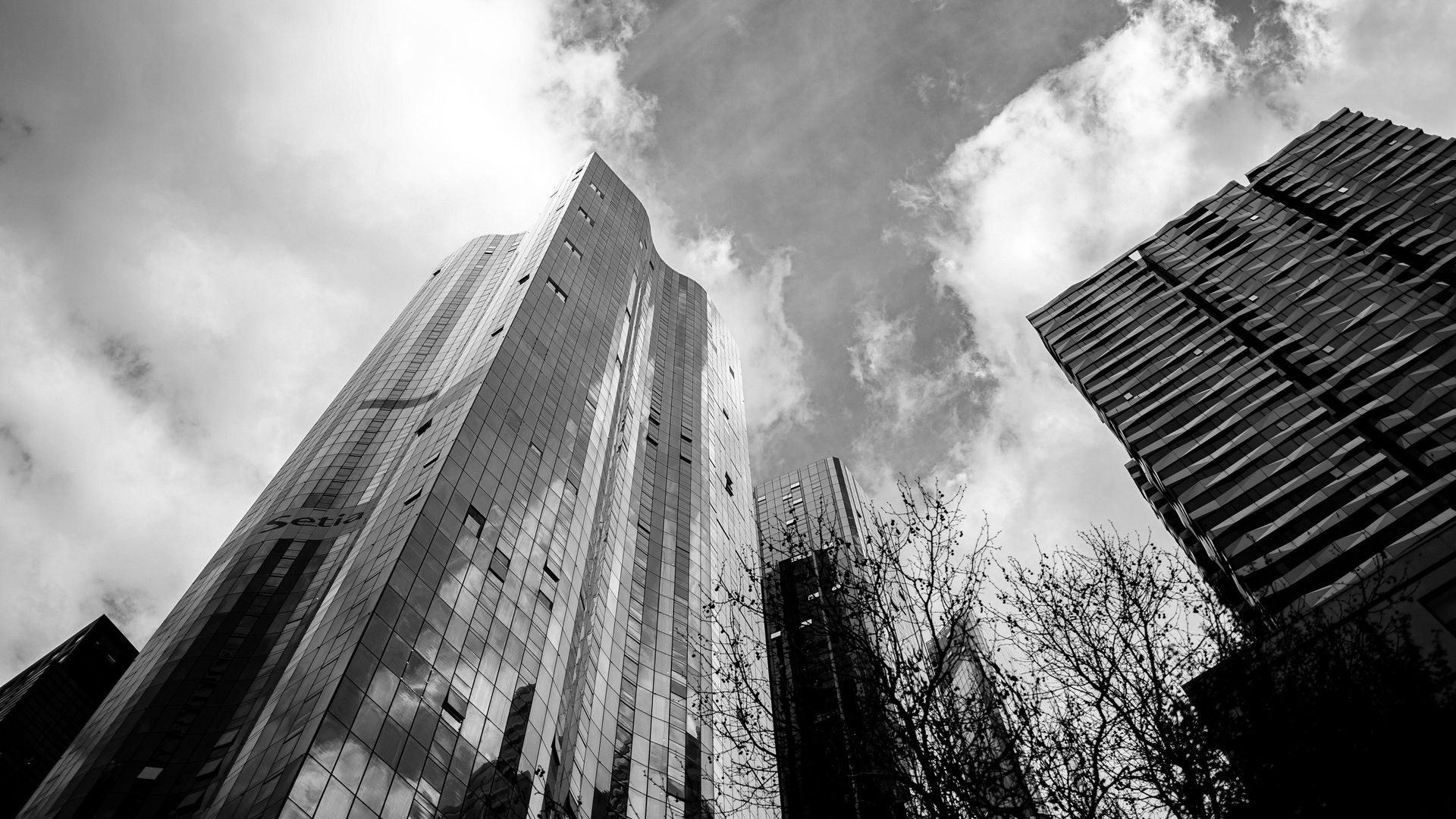 Black-and-white view of tall skyscrapers from below against a cloudy sky