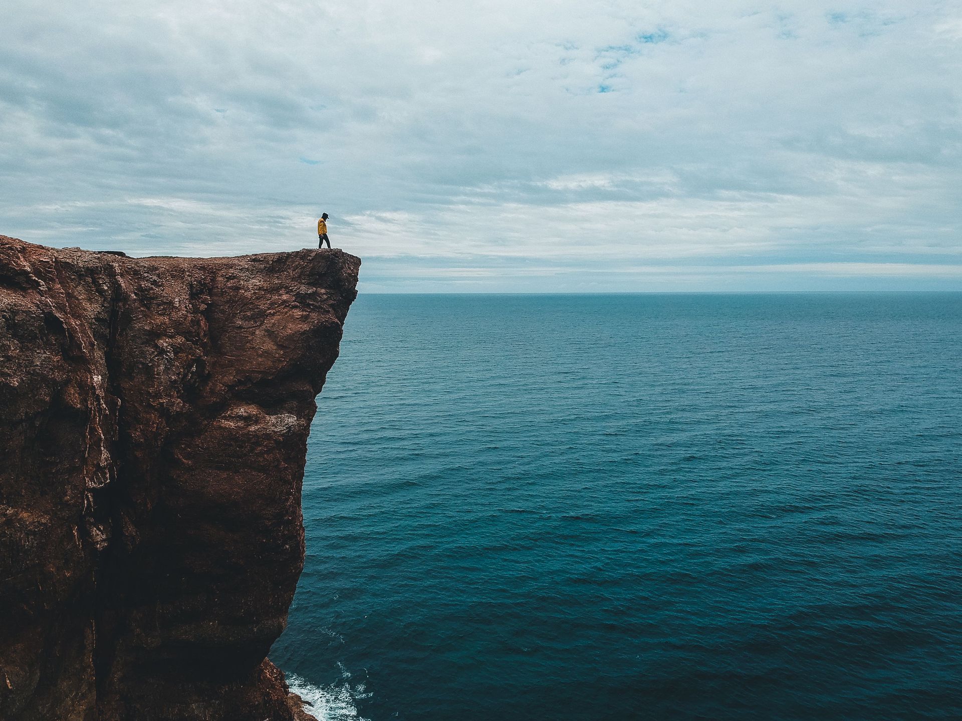 Person standing on a cliff overlooking the ocean, representing vision, innovation and new opportunit
