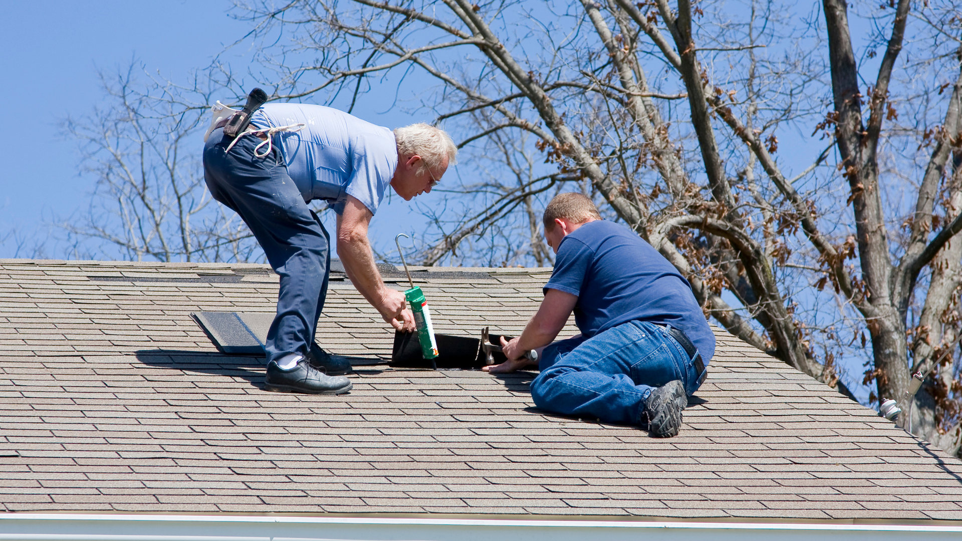 Two men are working on the roof of a house.