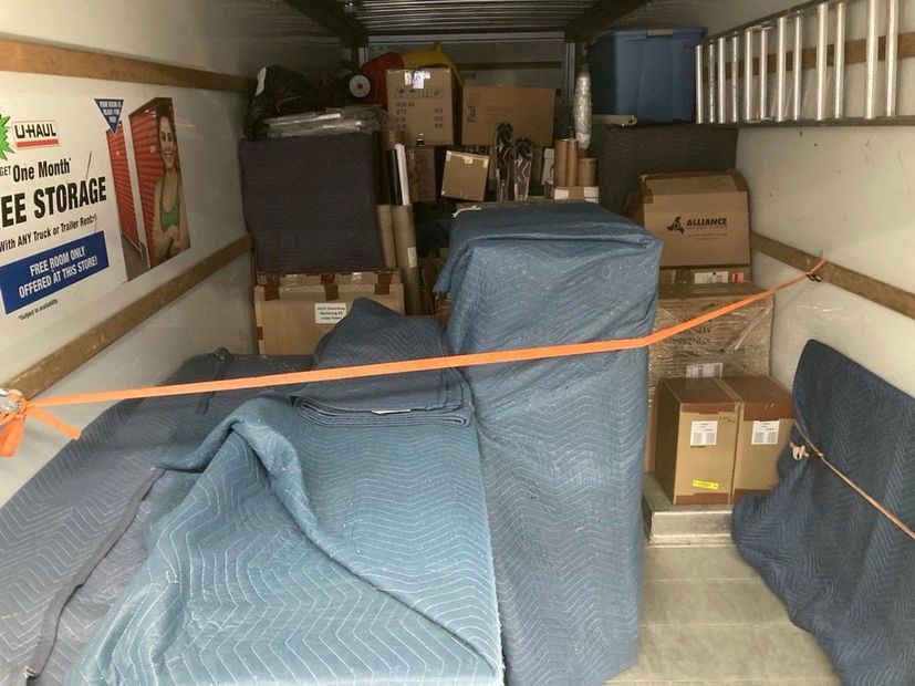 Packed storage truck with boxes and furniture wrapped in moving blankets and secured by orange straps