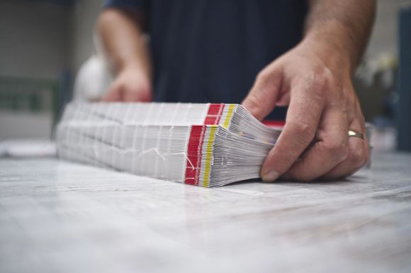 Mani di una persona che regge una pila di fogli avvolti nella plastica e fissati con nastro adesivo rosso e giallo.