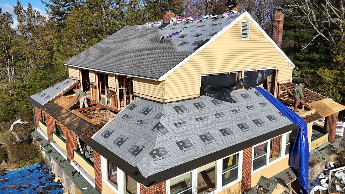 House roof being replaced with new shingles, with a blue tarp on the side and exposed roof deck.