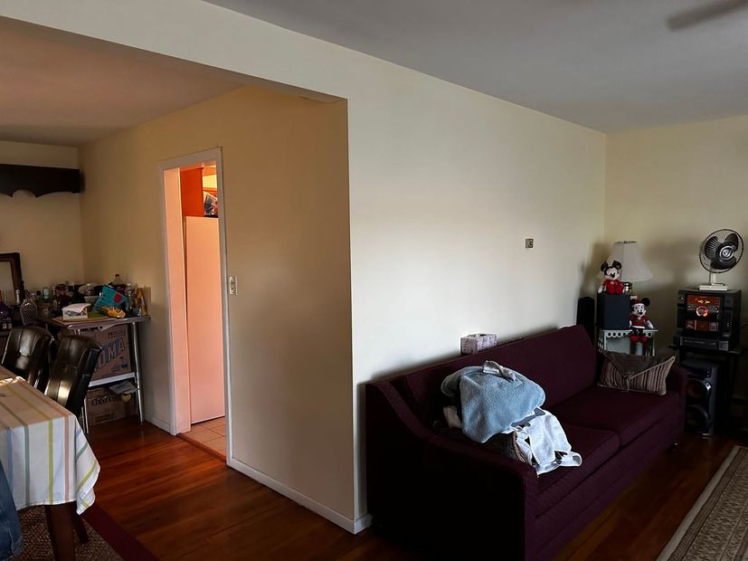 Living room with maroon couch, hardwood floor, and open doorway into a lit kitchen