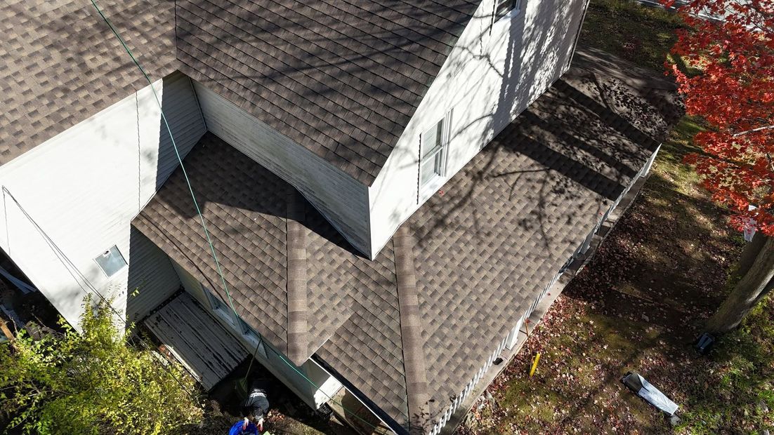 Aerial view of a house roof with a small porch, surrounding trees, and a driveway below.