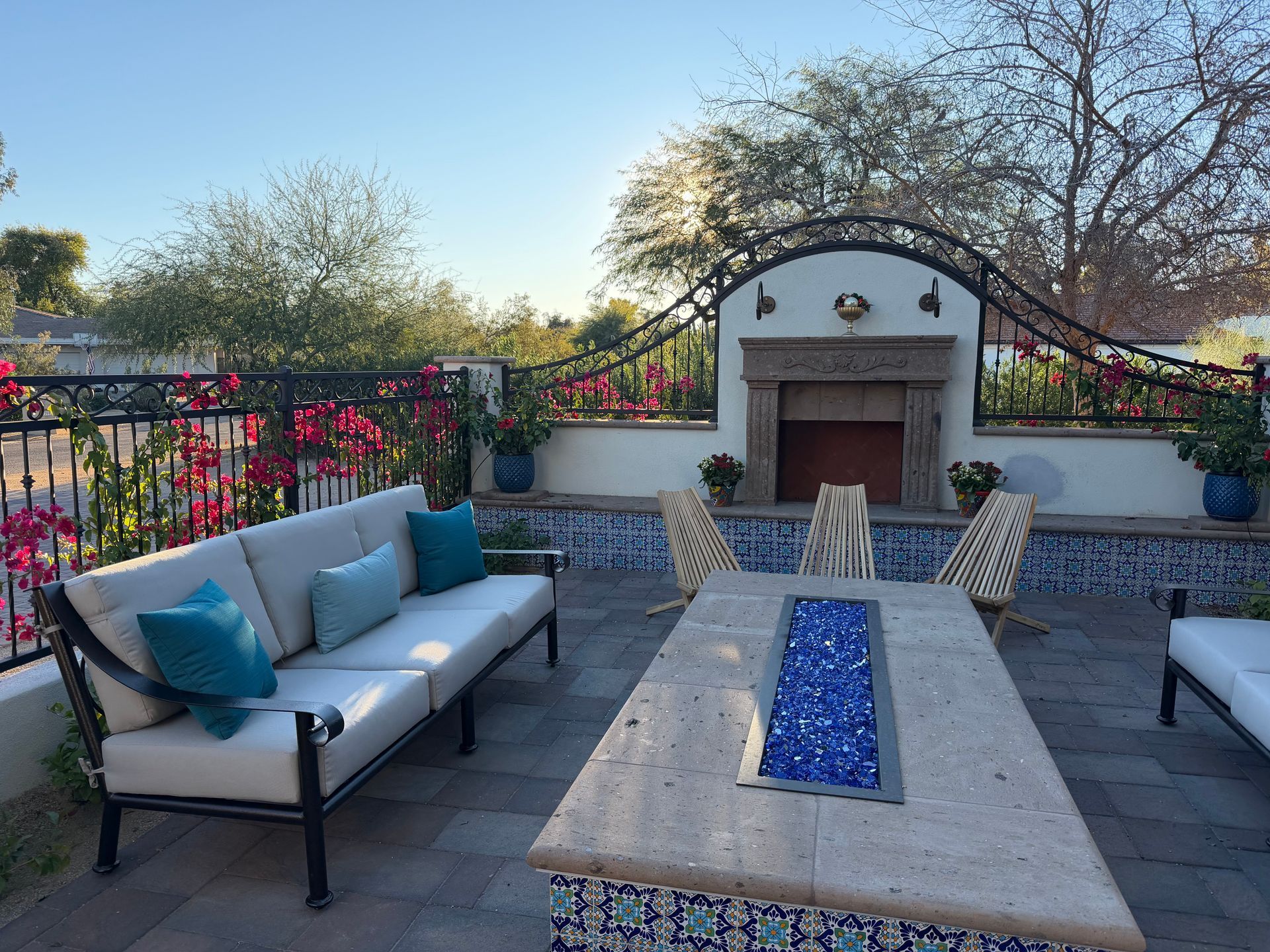 Patio seating area with outdoor sofa, fire pit table, and fireplace at sunset