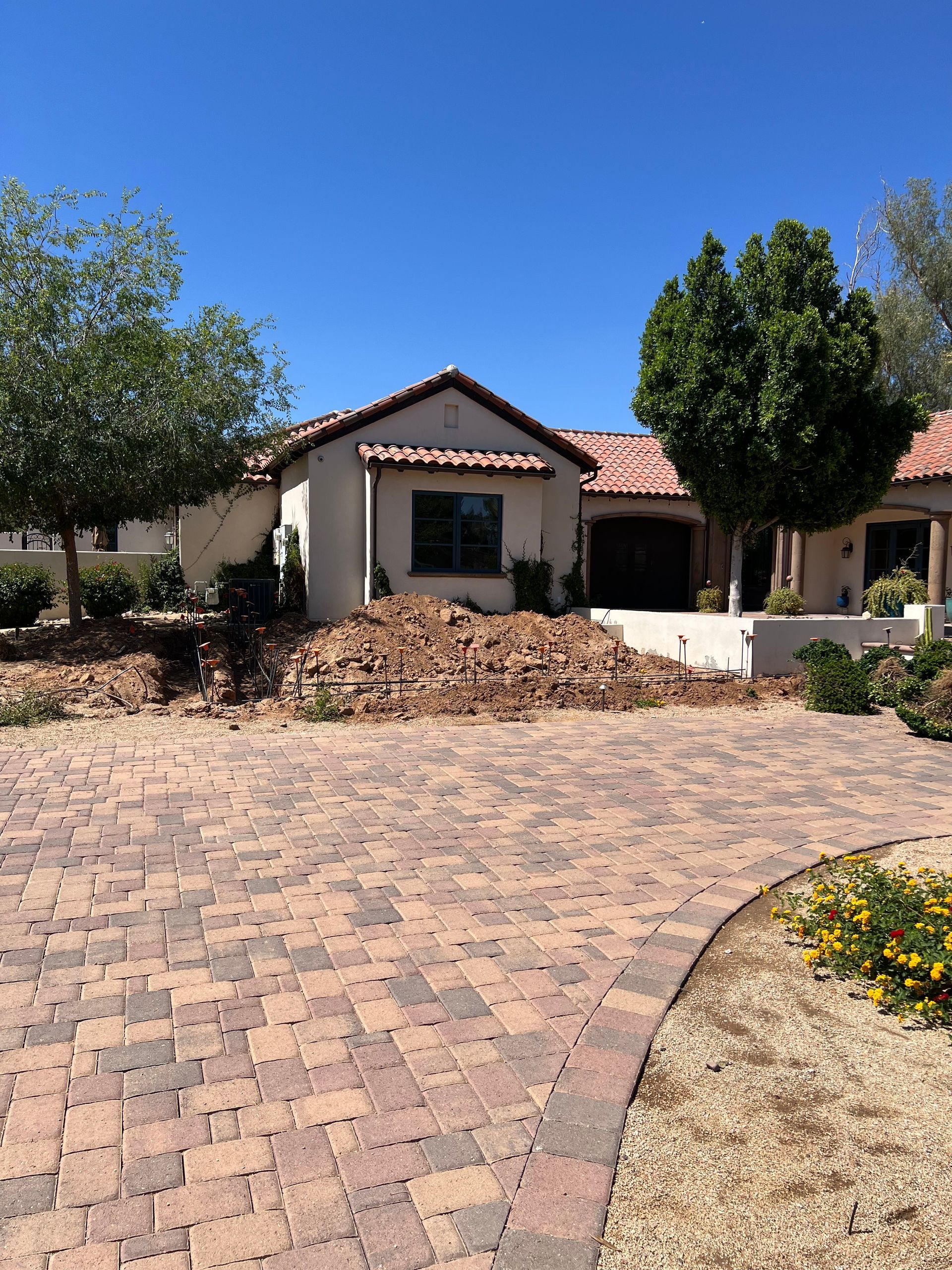 Single-story house with a red tile roof, brick driveway, and trees under a clear blue sky