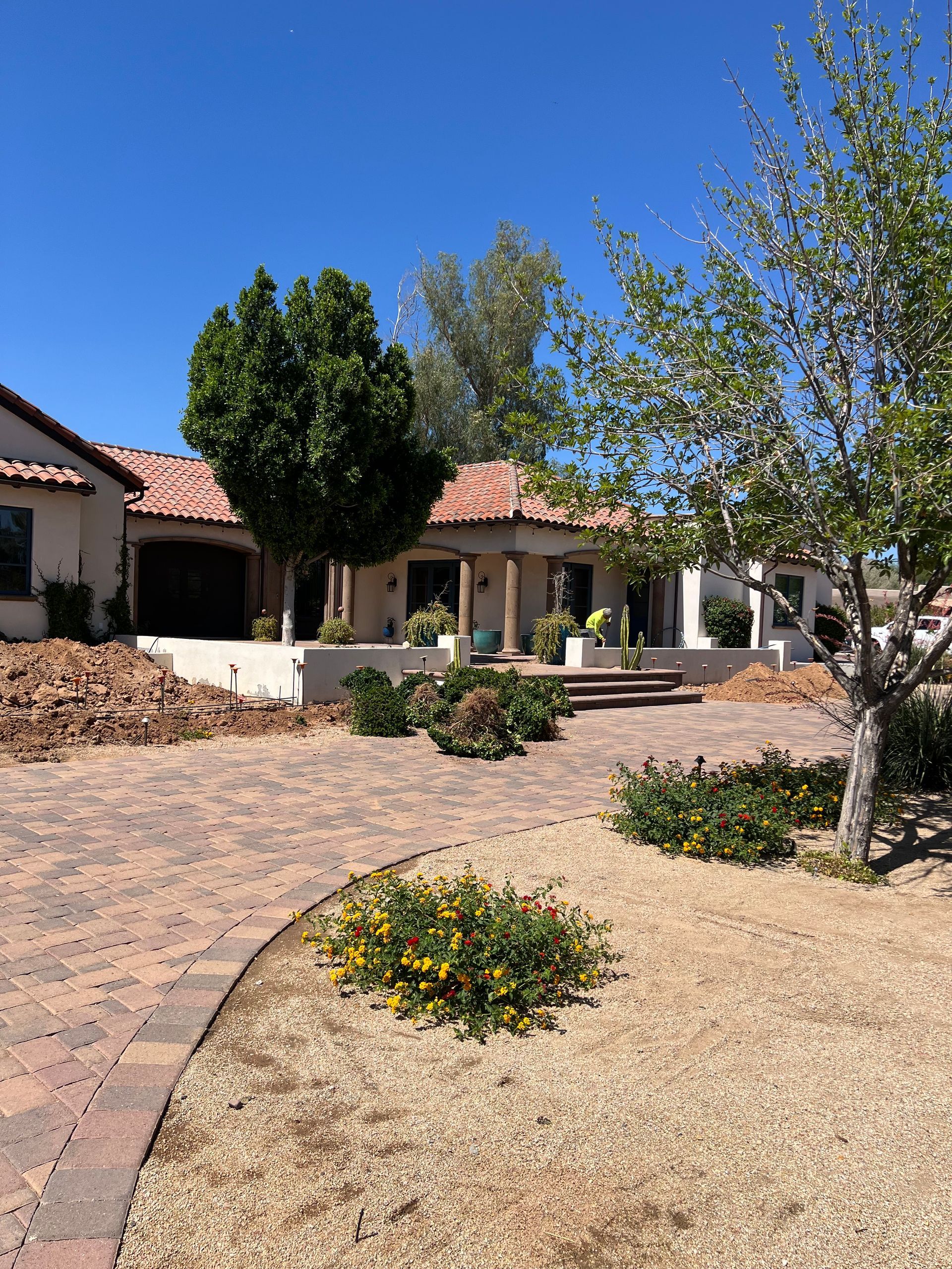 Sunlit courtyard with a stucco house, red-tile roof, paved walkway, and desert landscaping.
