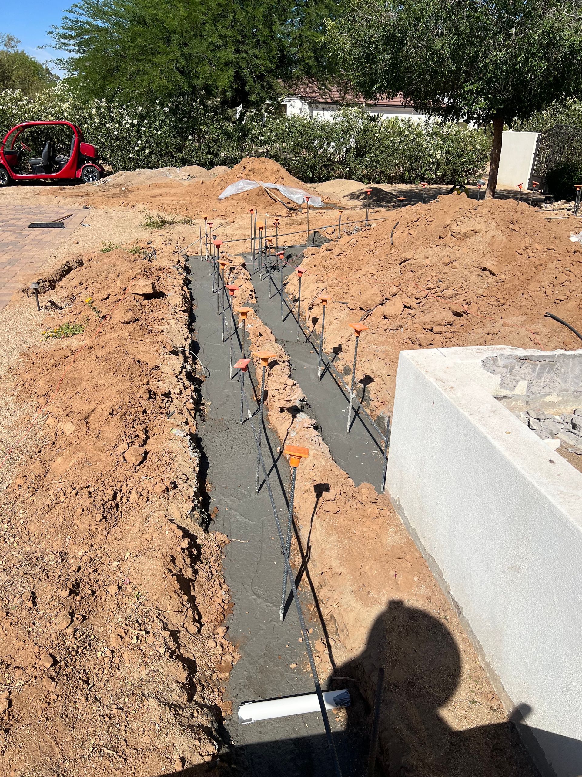 Backyard trench with black pipe under construction beside a concrete block wall and soil piles