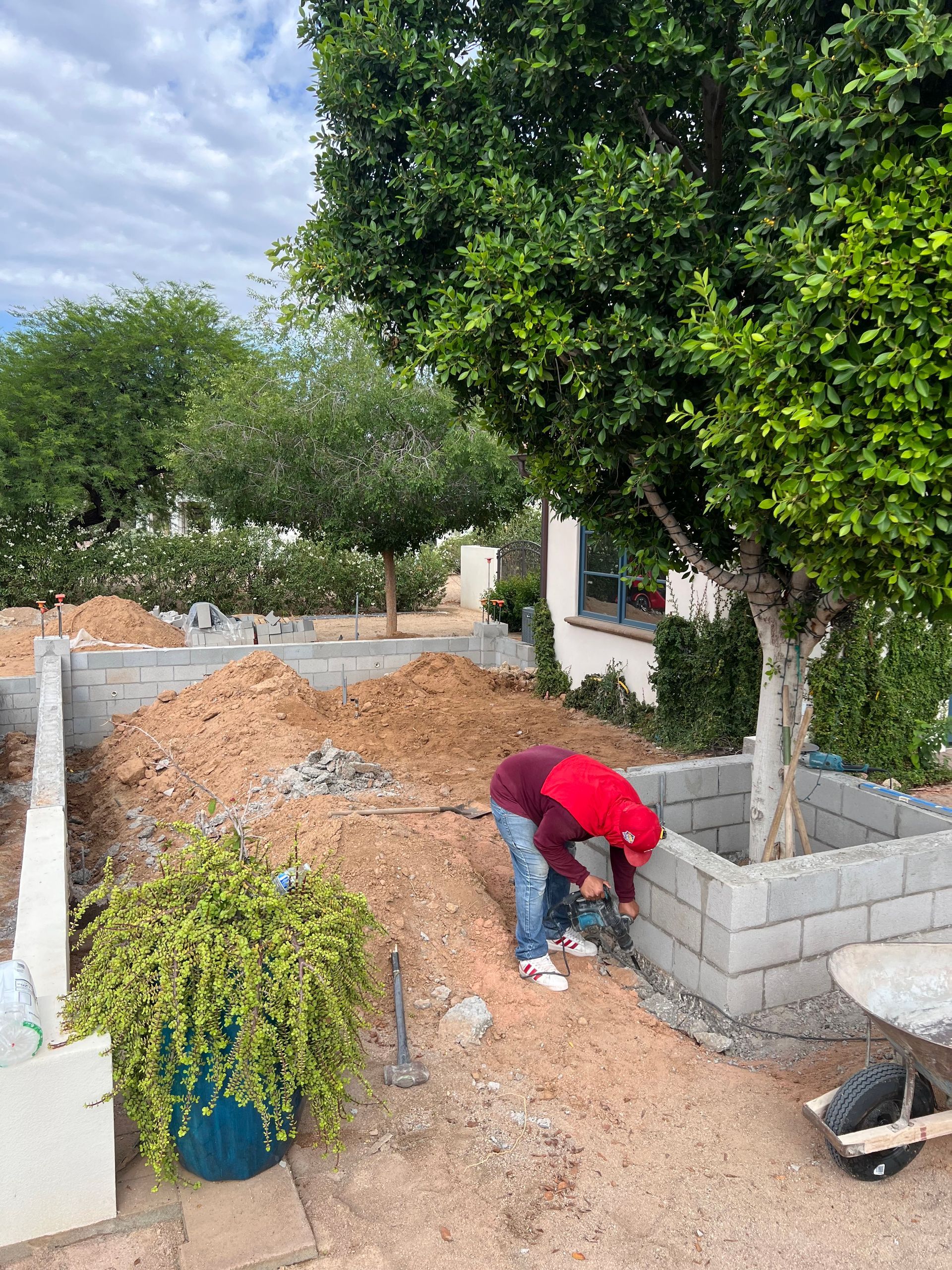 Worker bending over beside gravel path and cinder block wall in a garden under cloudy sky