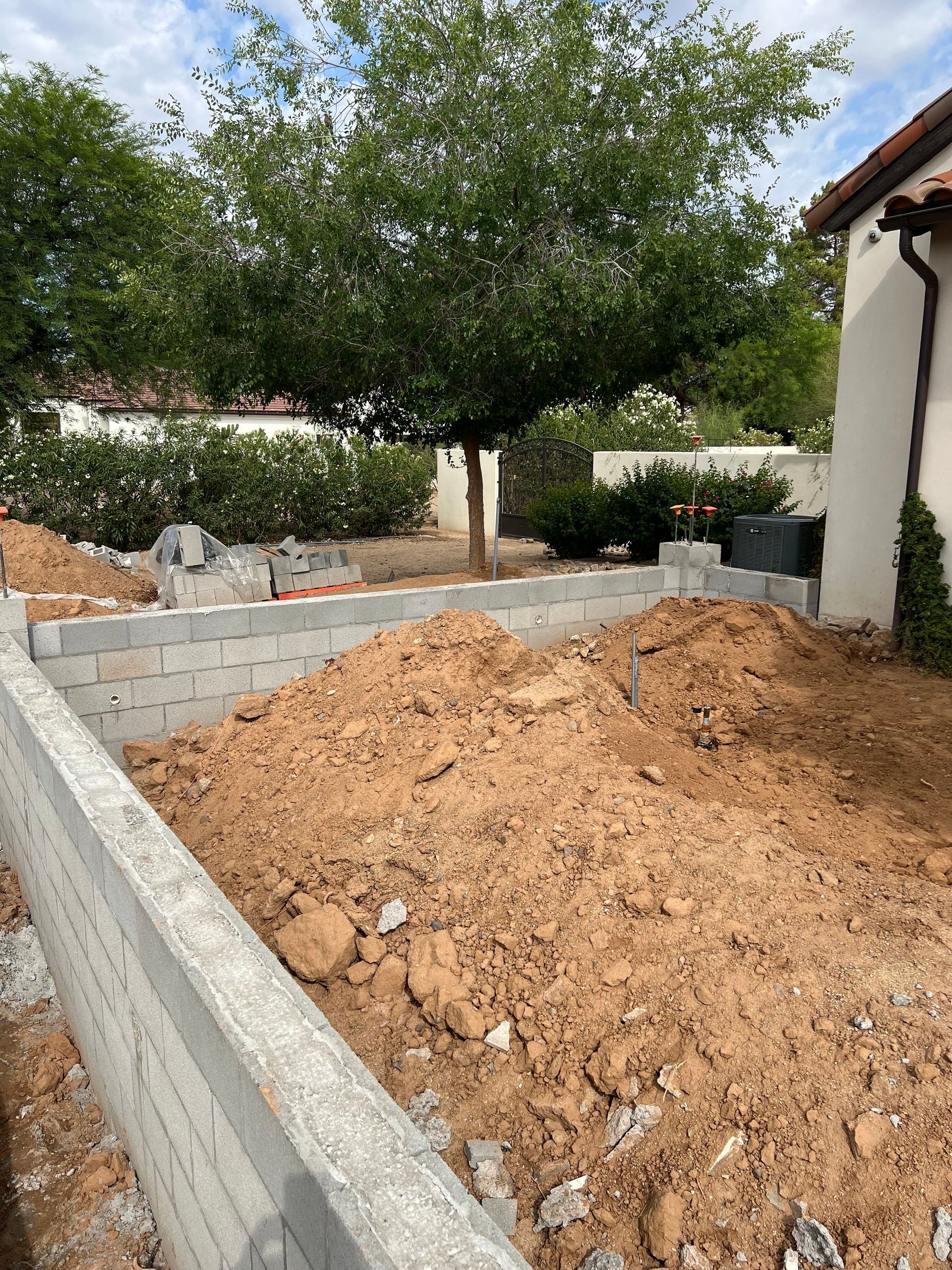 Backyard garden with raised concrete beds, soil mound, and trees beside a house