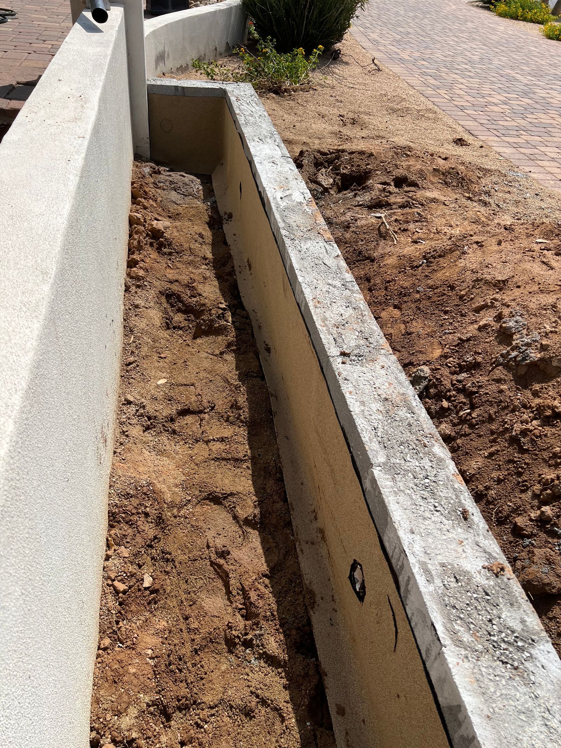 Concrete drainage channel beside a gravel path and retaining wall in a landscaped area