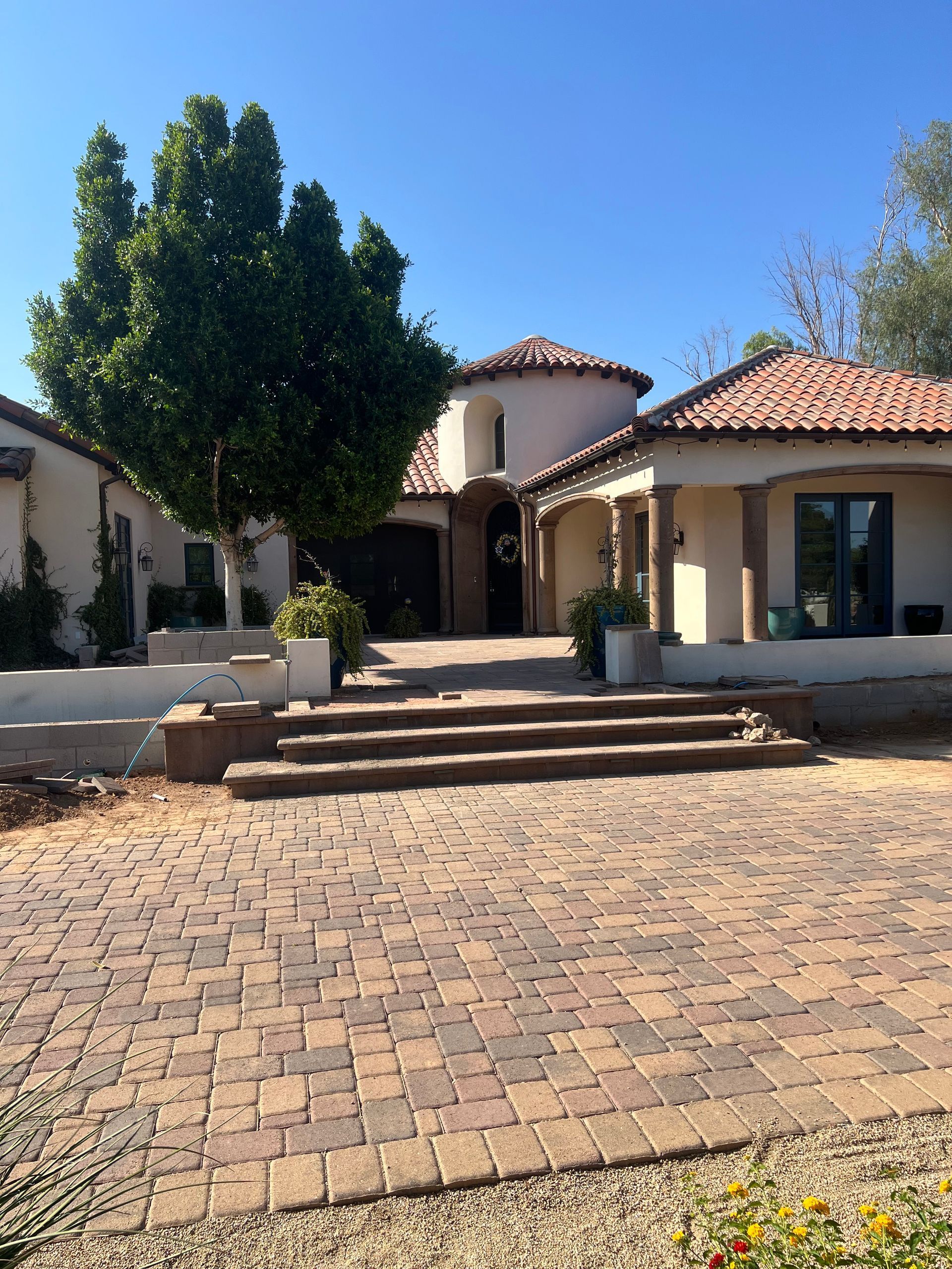 Mediterranean-style house with red tile roof, steps, and brick driveway under a clear blue sky