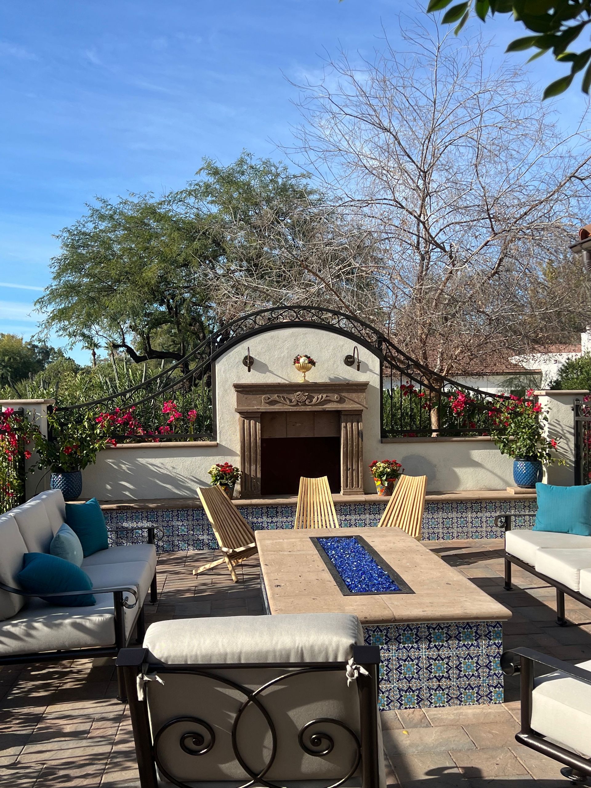 Patio with wicker seating, blue cushions, fire pit, and tiled outdoor fireplace under a tree