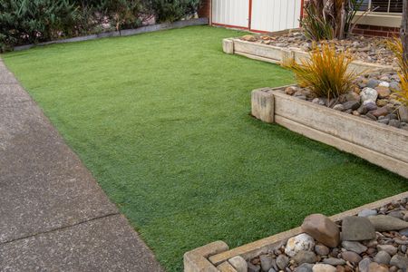 Neatly trimmed green lawn beside a concrete walkway and raised garden beds with rocks and ornamental plants.