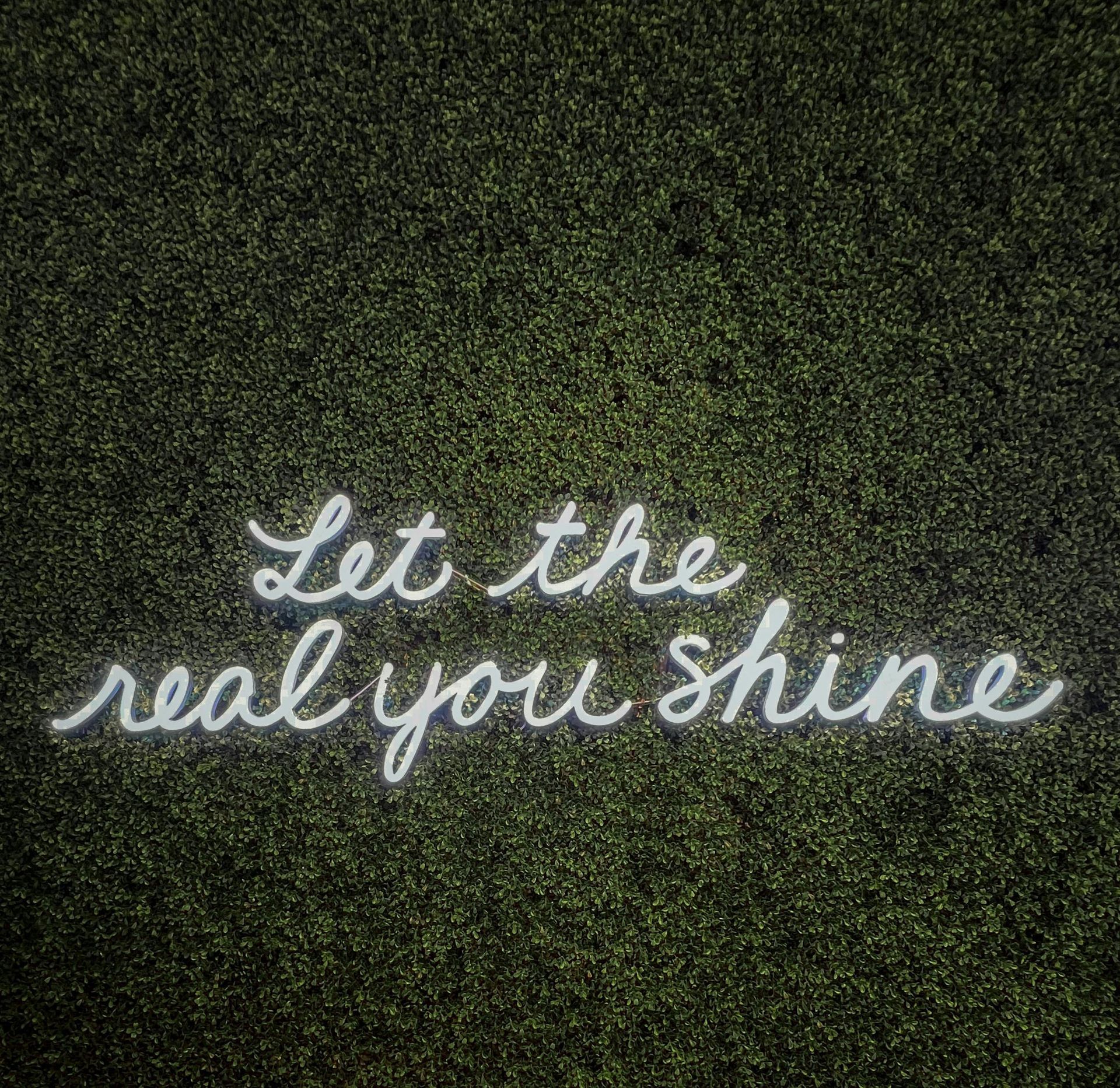 White script reading “Let the real you shine” on a dark green textured background