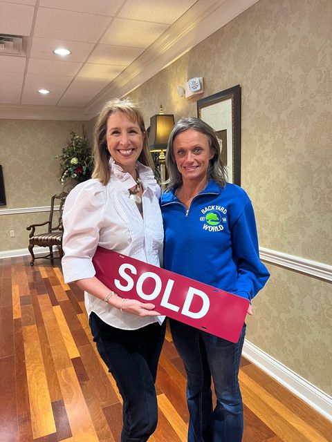 Two women holding a red “SOLD” sign in a hallway at an event.