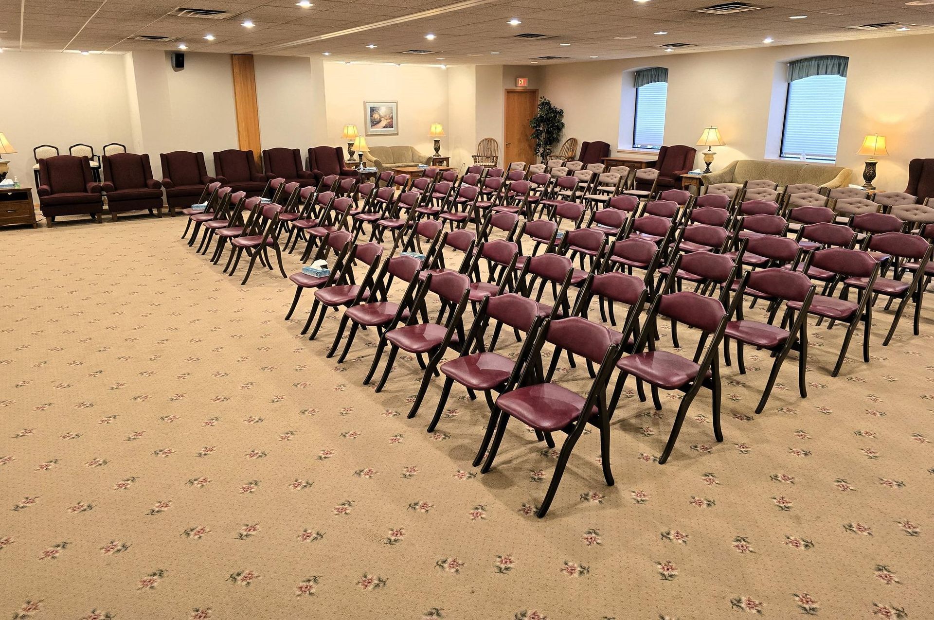A spacious, carpeted room set up for a presentation with rows of purple folding chairs facing a vacant front area.